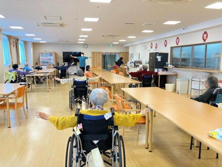 介護施設での集団活動。車椅子の入居者が参加する運動やレクリエーションの風景。