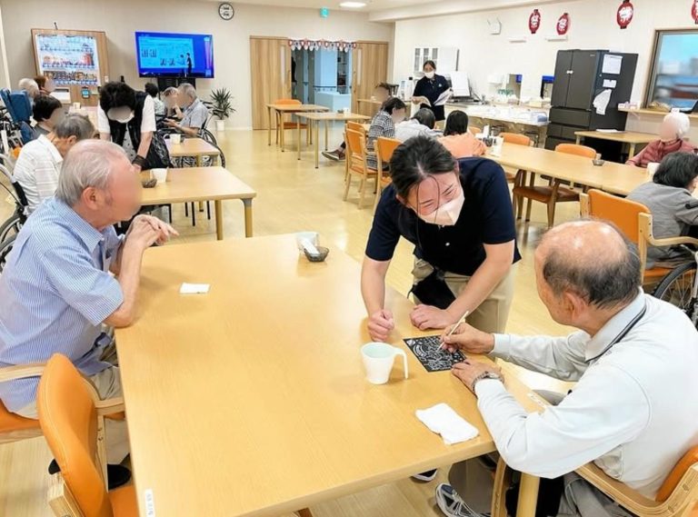 介護施設の共用スペースで入居者がスタッフと手工芸活動に参加している風景